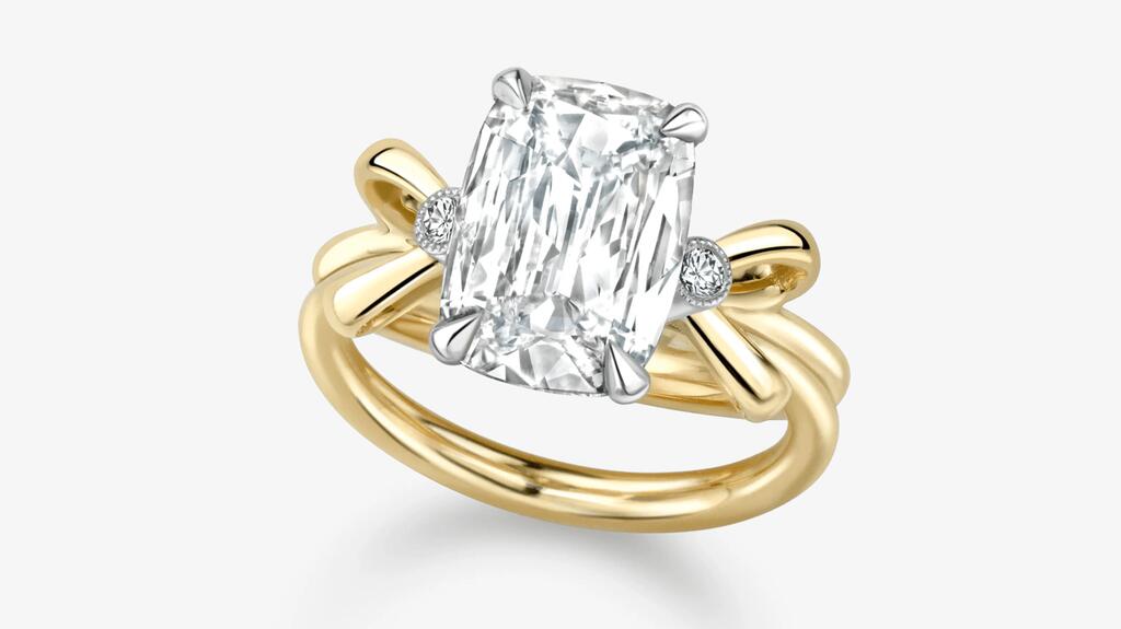 Une bague de fiançailles « Bows » centrant un diamant taille coussin de 3,03 carats dans une monture griffe en or blanc 18 carats flanquée de deux diamants plus petits et d'un motif nœud en or jaune 18 carats (prix sur demande) Jessica McCormack Bows Bague de fiançailles en diamant taille coussin